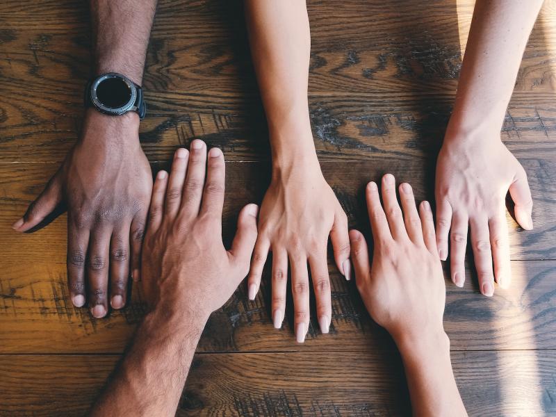 Five hands laying on a wooden table